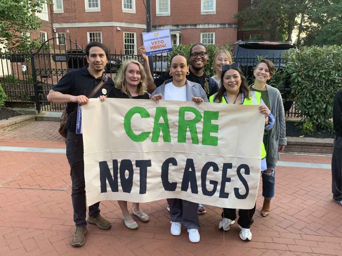 ACLU of Maryland staff members hold a banner that says, "Care Not Cages." They are outside in Lawyer's Mall for a rally asking Governor Moore to veto HB 814.