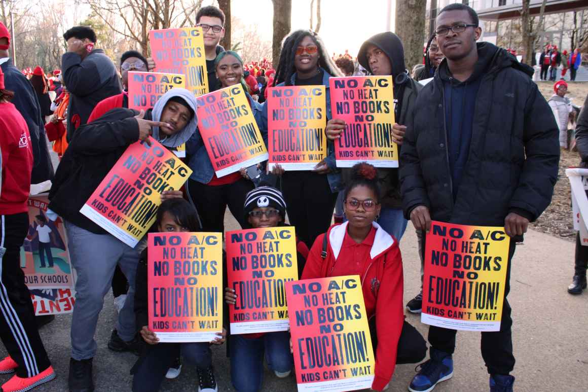 A group of students at Wide Angle Youth Media attend the March for Our Schools rally in Annapolis, Maryland. The students are holding posters they designed that are red and yellow gradient and say, "No A/C, no heat, no books, no education."