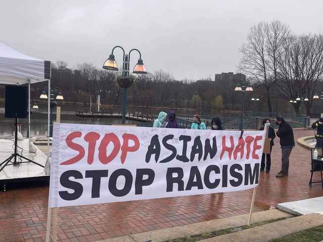  "Stop Aisan Hate - Stop Racism" banner on a rainy brick sidewalk.