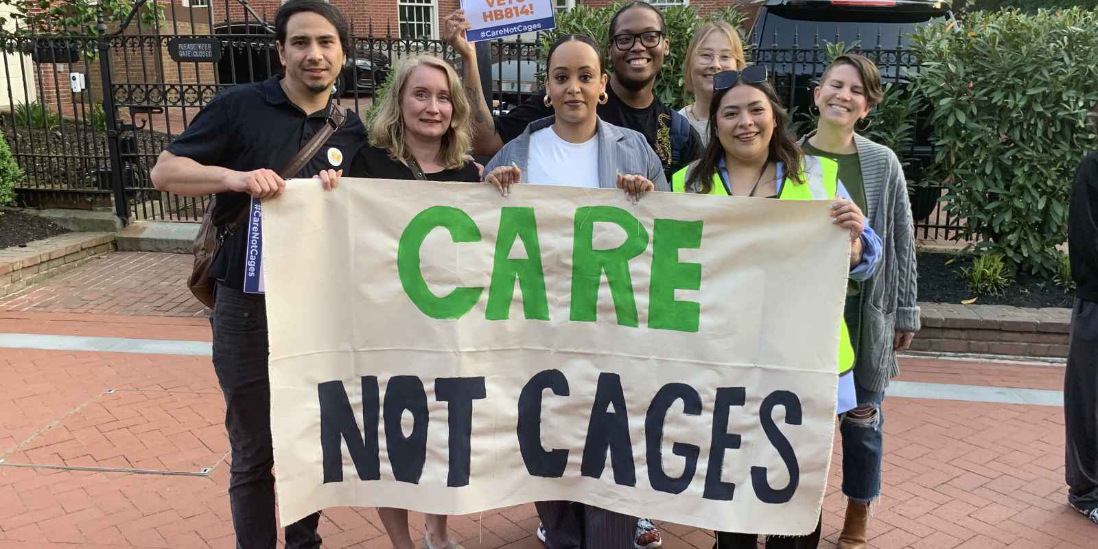 ACLU of Maryland staff members hold a banner that says, "Care Not Cages." They are outside in Lawyer's Mall for a rally asking Governor Moore to veto HB 814.