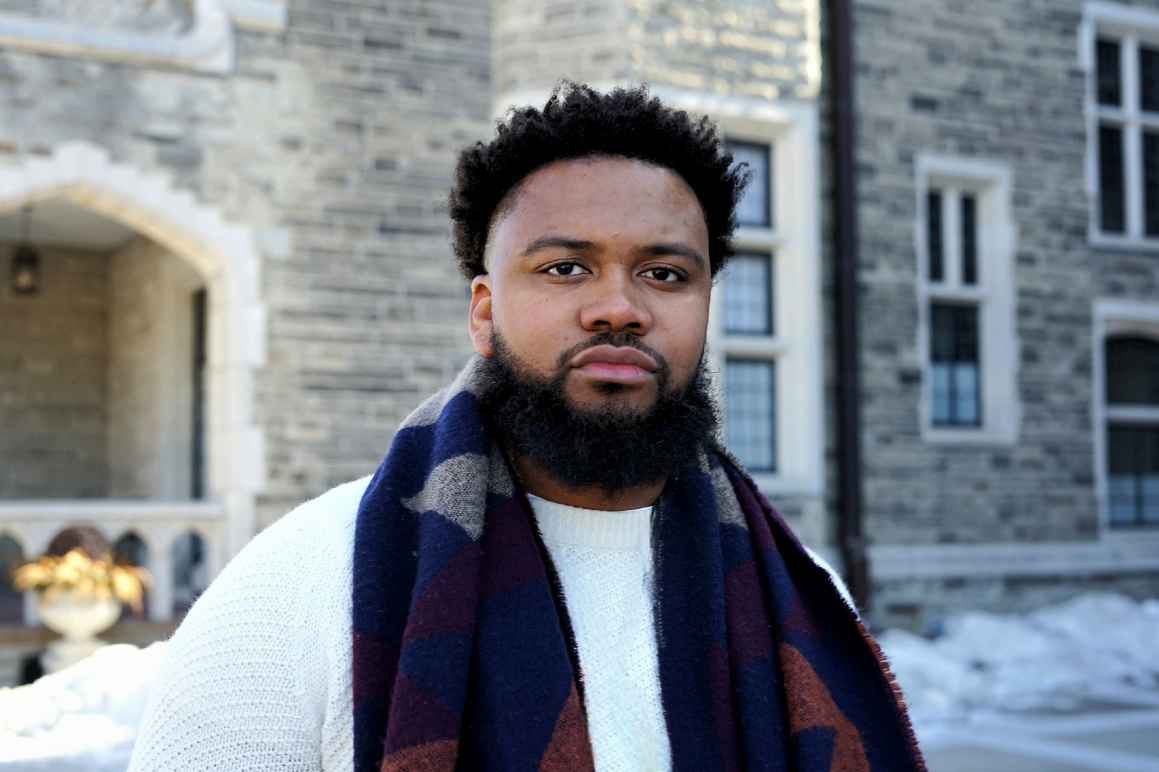 Nehemiah Bester is a Black man with short hair and a beard, and is wearing a light sport jacket, light collared shirt, and burguny tie.